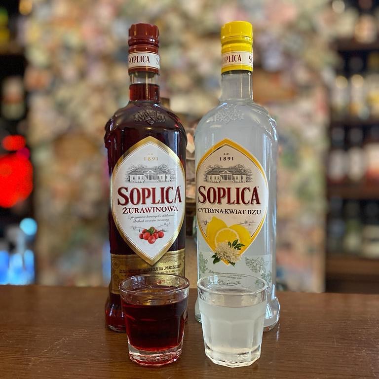 Two bottles of Soplica Zurawinowa and two shots in front of them. Different flavors.